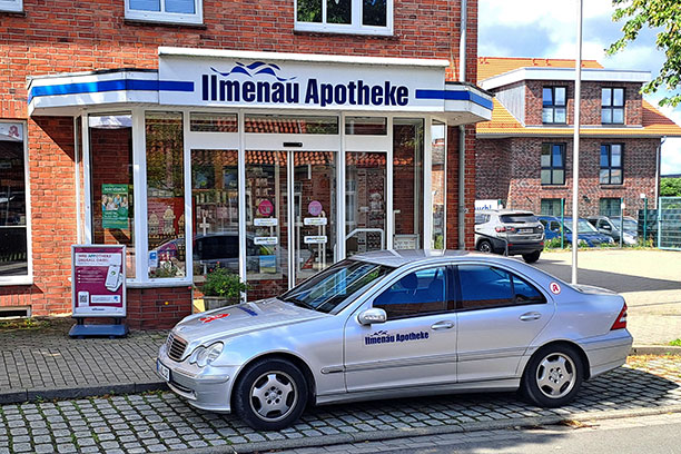 Silberner PKW mit Apothekenaufklebern vor der Apotheke